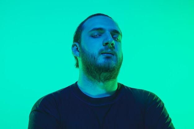 Portrait of a guy with colorful neon light on green  wall. Male model with calm and serious mood. Facial expression, millenials lifestyle and look like. Future, technologies.