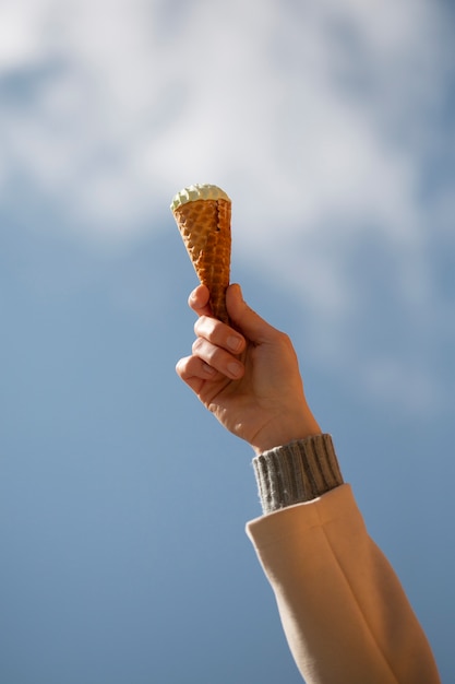 Portrait of hand holding ice cream cone against sky