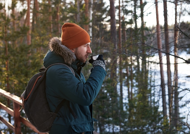 Portrait of handsome bearded man drinking hot tea outdoor in forest trip on foot