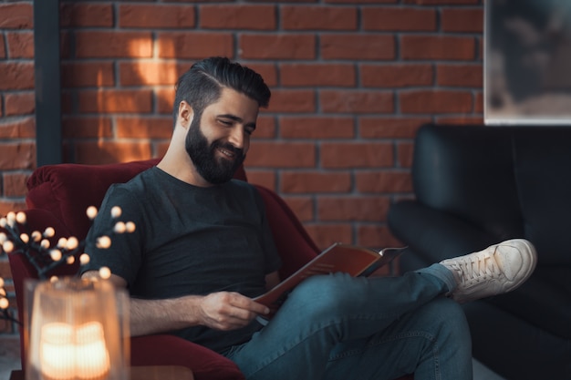 Free Photo portrait handsome bearded man wearing casual clothing, sitting in red chair modern loft