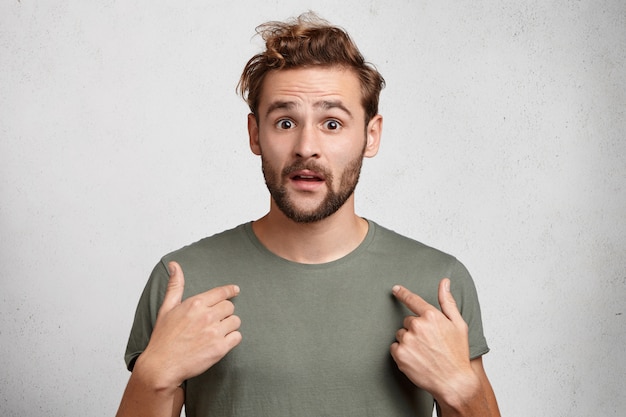 Free photo portrait of handsome bearded young man points at himself being puzzled to be chosen