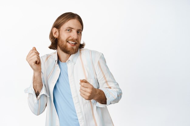 Portrait of handsome blond bearded guy, dancing carefree, smiling joyful, standing in casual outfit on white. Copy space