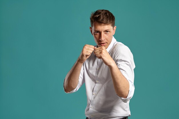 Portrait of a handsome brunet man with brown eyes, wearing in a classic white shirt. He is acting like he is fighting while posing in a studio against a blue background. Concept of gesticulation and s