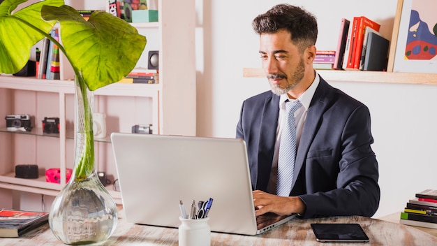 Portrait of handsome businessman using laptop at his workplace