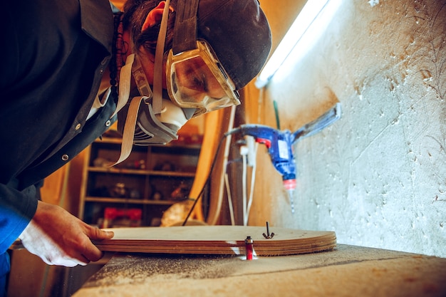 Portrait of handsome carpenter working with wooden skate at workshop, profile view