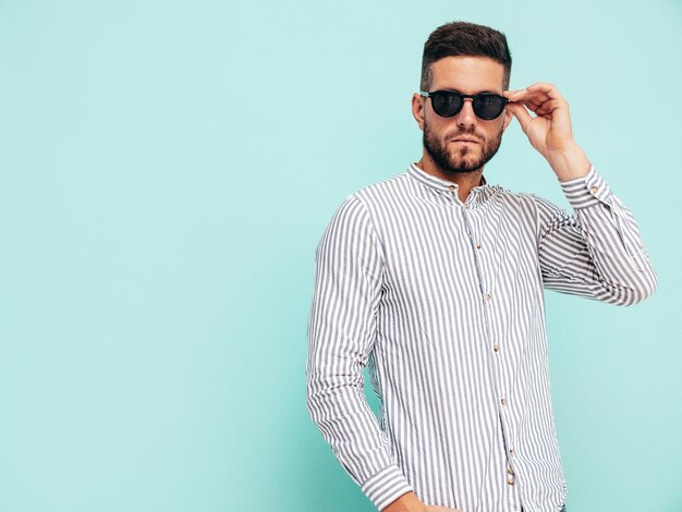 Portrait of handsome confident model Sexy stylish man dressed in shirt and jeans Fashion hipster male posing near blue wall in studio