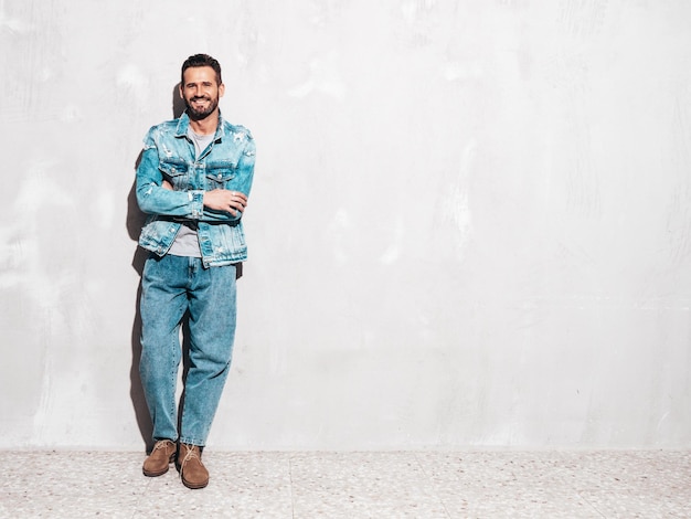 Free Photo portrait of handsome confident stylish hipster lambersexual model sexy man dressed in jeans jacket fashion male isolated on white wall in studio