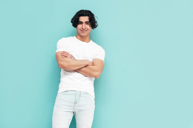 Portrait of handsome confident stylish hipster lambersexual model Sexy man dressed in summer white Tshirt and jeans clothes Fashion male isolated in studio Posing near blue wall