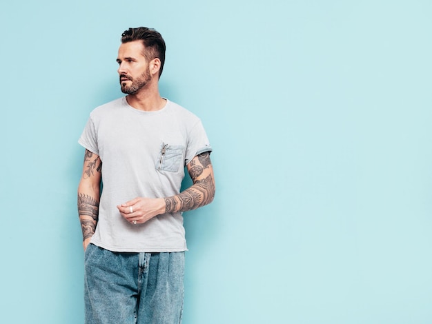 Portrait of handsome confident stylish hipster lambersexual model Sexy man dressed in Tshirt and jeans Fashion male isolated on blue wall in studio