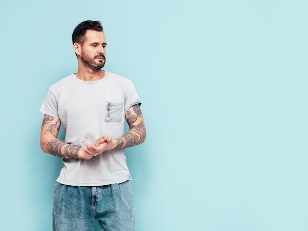 Portrait of handsome confident stylish hipster lambersexual model Sexy man dressed in Tshirt and jeans Fashion male isolated on blue wall in studio