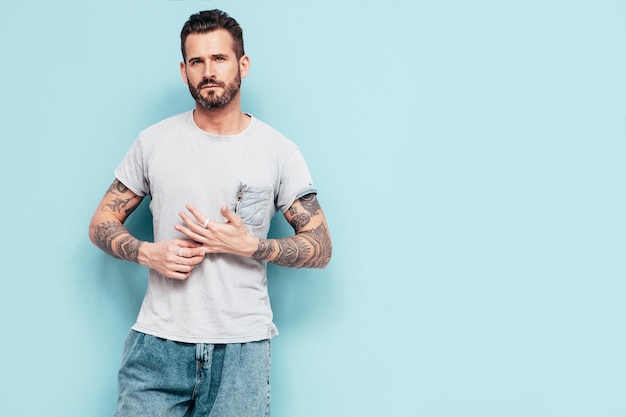 Free photo portrait of handsome confident stylish hipster lambersexual model sexy man dressed in tshirt and jeans fashion male isolated on blue wall in studio