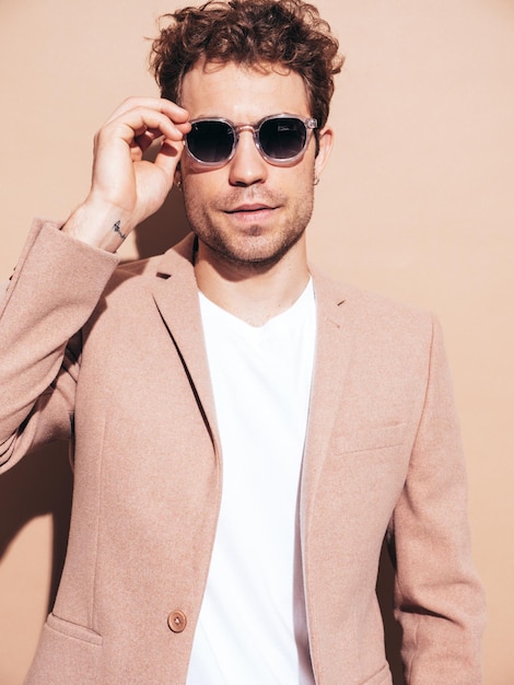 Portrait of handsome confident stylish hipster lambersexual model Sexy modern man dressed in elegant beige suit Fashion male with curly hairstyle posing in studio Isolated In sunglasses