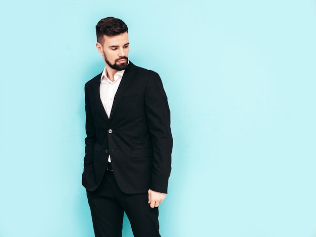 Free Photo portrait of handsome confident stylish hipster lambersexual model sexy modern man dressed in elegant black suit fashion male posing in studio near blue wall