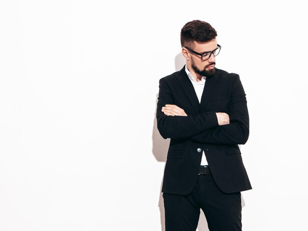 Portrait of handsome confident stylish hipster lambersexual model Sexy modern man dressed in elegant black suit Fashion male posing in studio near white wall Isolated