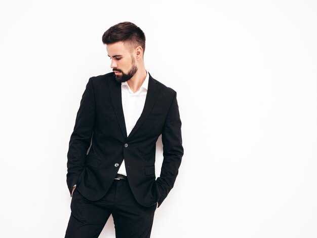 Free Photo portrait of handsome confident stylish hipster lambersexual model sexy modern man dressed in elegant black suit fashion male posing in studio near white wall isolated