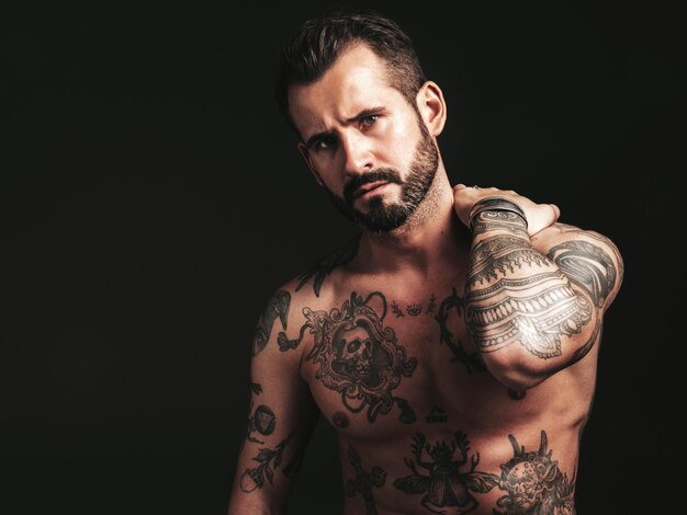 Portrait of handsome confident stylish hipster lambersexual model Sexy modern man Naked torso with tattoosFashion male posing in studio on dark background