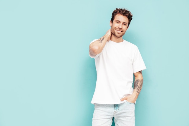 Free Photo portrait of handsome confident stylish hipster lambersexual model with curly hairstyle sexy man dressed in jeans and white tshirt fashion male isolated on blue wall in studio