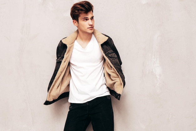 Portrait of handsome confident stylish hipster lambersexual modelMan dressed in black jacket and jeans Fashion male posing in studio near grey wall