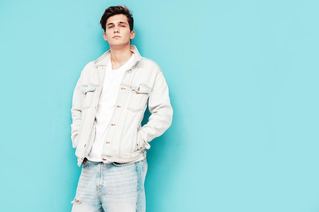 Free Photo portrait of handsome confident stylish hipster lambersexual modelman dressed in jacket and jeans fashion male posing in studio near blue wall