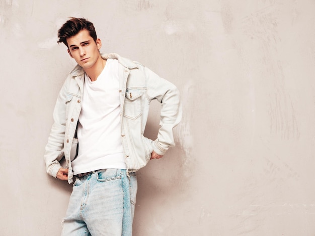 Portrait of handsome confident stylish hipster lambersexual modelMan dressed in jacket and jeans Fashion male posing in studio near grey wall