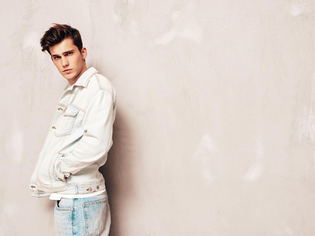 Portrait of handsome confident stylish hipster lambersexual modelMan dressed in jacket and jeans Fashion male posing in studio near grey wall