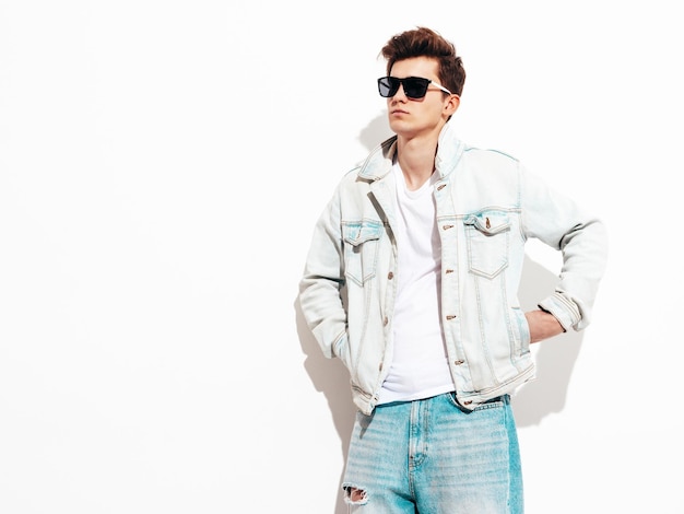 Portrait of handsome confident stylish hipster lambersexual modelMan dressed in jacket and jeans Fashion male posing in studio near white wall