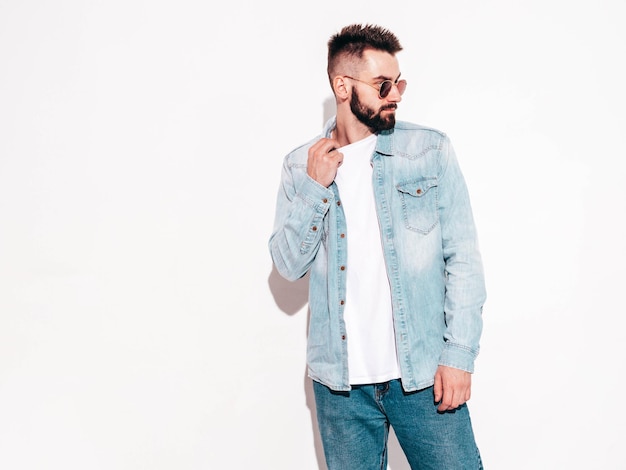 Portrait of handsome confident stylish hipster lambersexual modelMan dressed in jacket and jeans Fashion male posing in studio in sunglasses Isolated on white