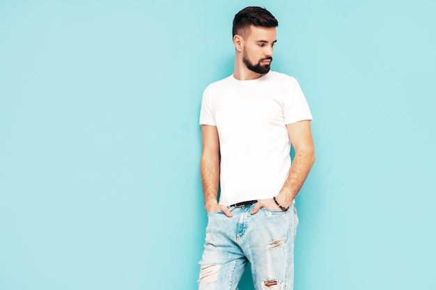 Portrait of handsome confident stylish hipster lambersexual modelMan dressed in white Tshirt and jeans Fashion male isolated on blue wall in studio