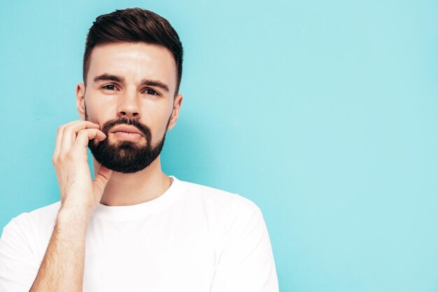 Portrait of handsome confident stylish hipster lambersexual modelMan dressed in white Tshirt and jeans Fashion male isolated on blue wall in studio