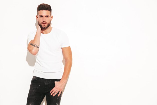 Portrait of handsome confident stylish hipster lambersexual modelMan dressed in white tshirt and jeans Fashion male posing near wall in studio Isolated