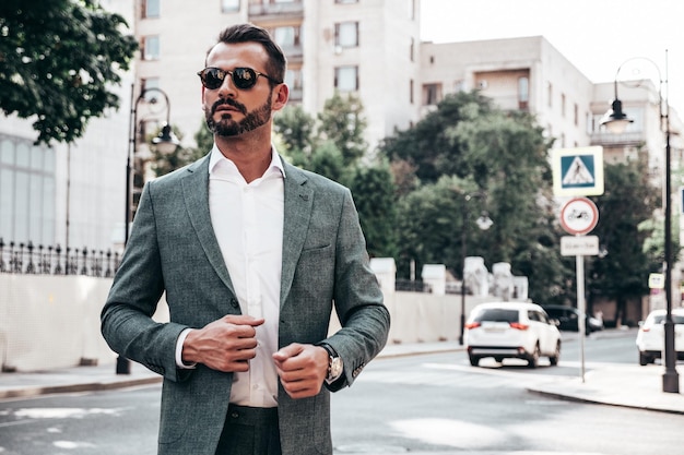 Free photo portrait of handsome confident stylish hipster lambersexual modelmodern man dressed in elegant suit fashion male posing in the street background in europe city at sunset in sunglasses