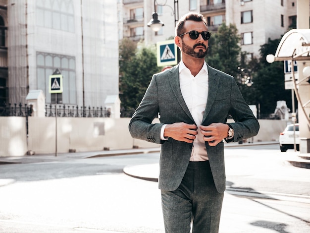 Free photo portrait of handsome confident stylish hipster lambersexual modelsexy modern man dressed in elegant suit fashion male posing in the street background in europe city at sunset in sunglasses