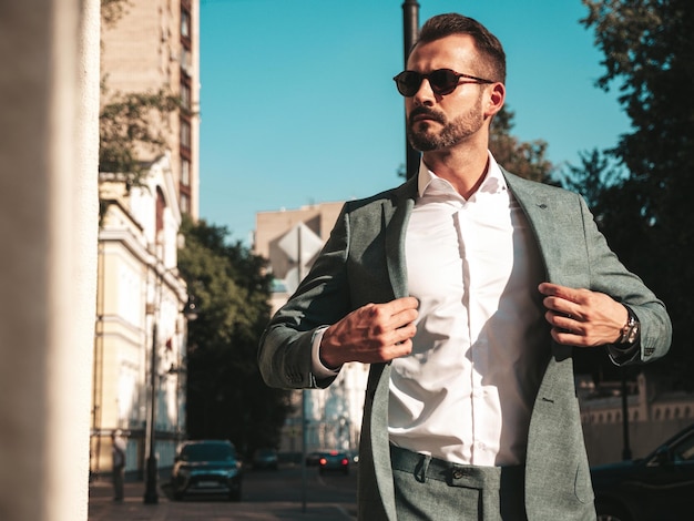 Free photo portrait of handsome confident stylish hipster lambersexual modelsexy modern man dressed in elegant suit fashion male posing in the street background in europe city at sunset in sunglasses