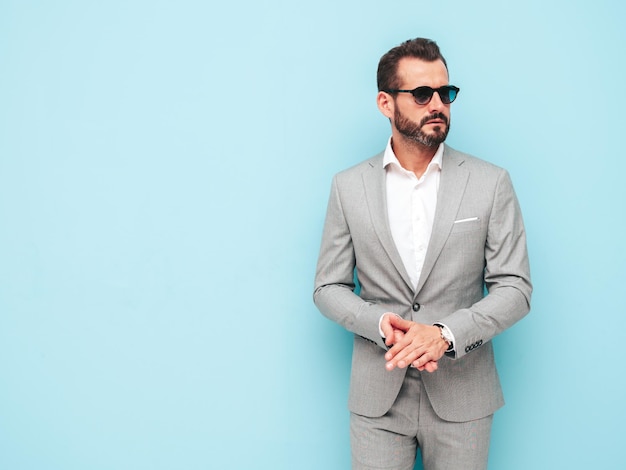 Free Photo portrait of handsome confident stylish hipster lambersexual modelsexy modern man dressed in elegant suit fashion male posing in studio near blue wall in sunglasses