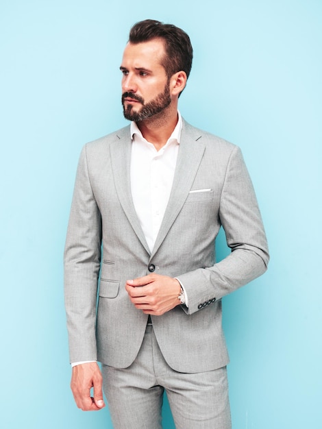 Portrait of handsome confident stylish hipster lambersexual modelSexy modern man dressed in elegant suit Fashion male posing in studio near blue wall