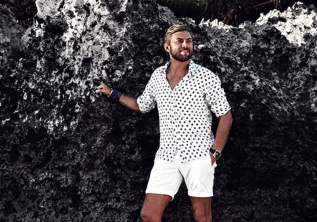 Free Photo portrait of handsome fashion man model wearing white clothes posing near rocks on the beach