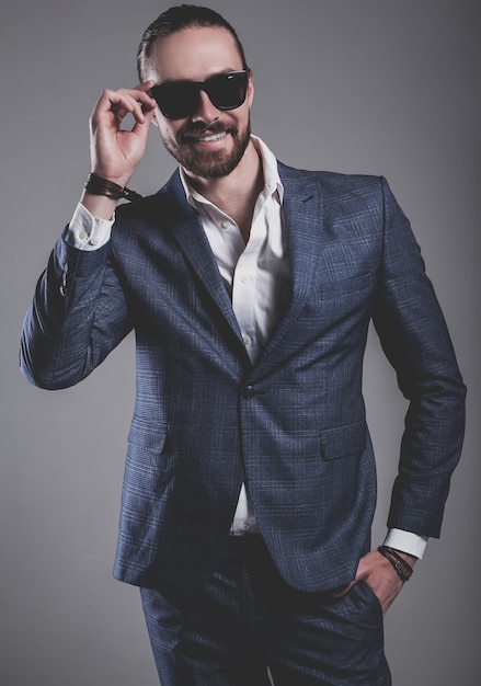 portrait of handsome fashion stylish hipster businessman model dressed in elegant blue suit posing on gray