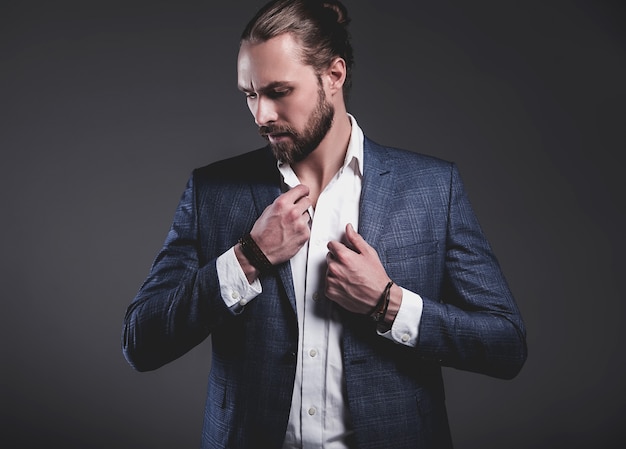 portrait of handsome fashion stylish hipster businessman model dressed in elegant blue suit posing on gray