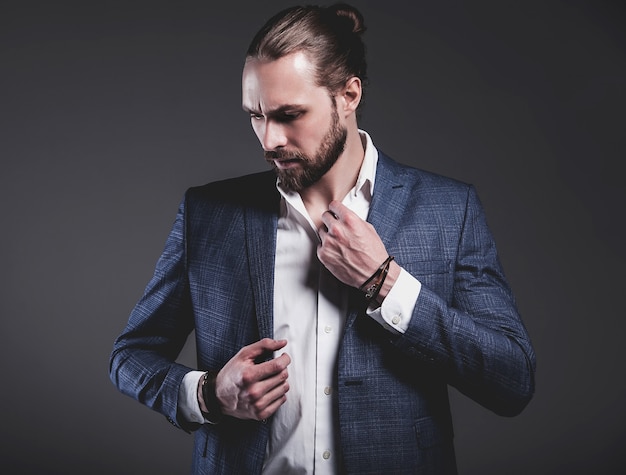 portrait of handsome fashion stylish hipster businessman model dressed in elegant blue suit posing on gray