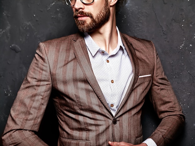 Free Photo portrait of handsome fashion stylish hipster businessman model dressed in elegant brown suit in glasses near dark wall