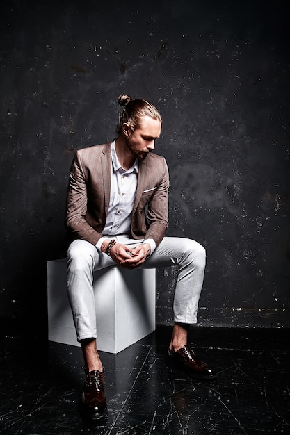 portrait of handsome fashion stylish hipster businessman model dressed in elegant brown suit sitting near dark