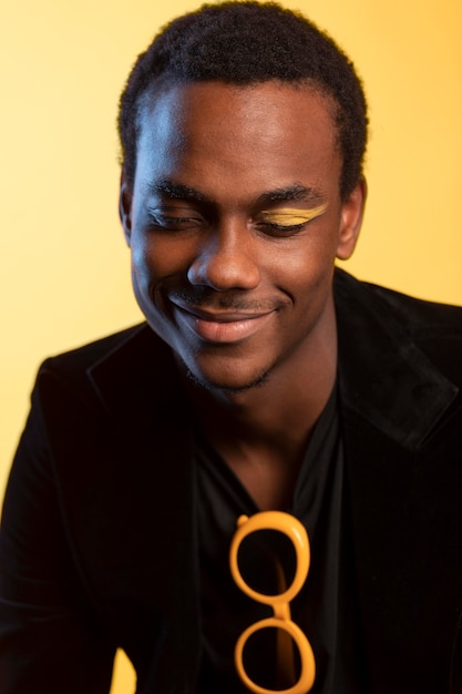 Free photo portrait of handsome man with sunglasses and eye make-up over yellow background