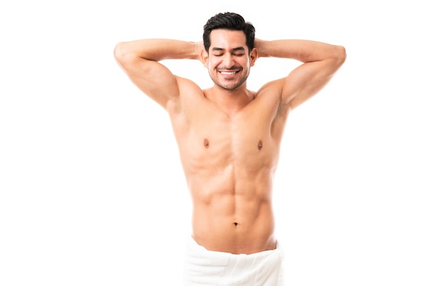 Portrait of a handsome muscular man standing with his hands behind his head and smiling on white background