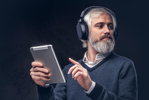 Free Photo portrait of a handsome senior man using a tablet with headphones in a studio over a dark background.