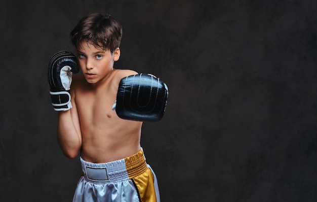 Portrait of a handsome shirtless young boxer wearing gloves, looking at a camera. Isolated on the dark background.