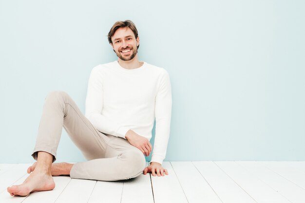 Portrait of handsome smiling hipster lumbersexual businessman model wearing casual white sweater and trousers