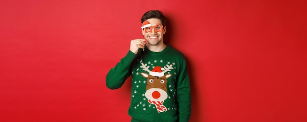 Free photo portrait of handsome smiling man in christmas sweater and party glasses celebrating new year and hav...