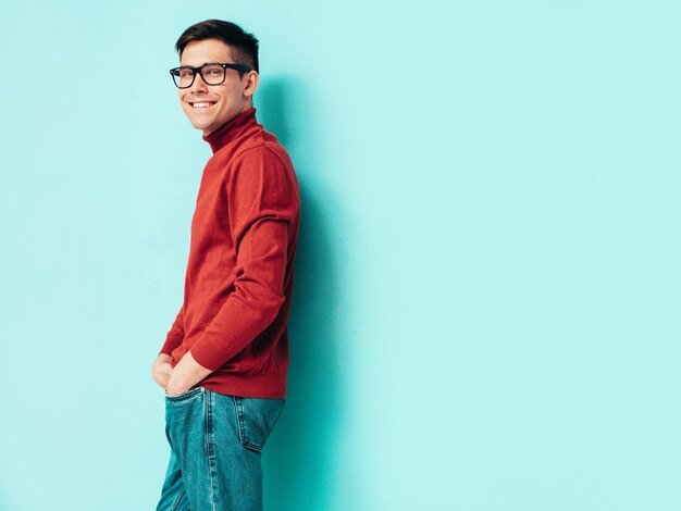 Portrait of handsome smiling model Sexy stylish man dressed in red turtleneck sweater and jeans Fashion hipster male posing near blue wall in studio Isolated