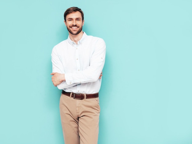 Portrait of handsome smiling model Sexy stylish man dressed in shirt and trousers Fashion hipster male posing near blue wall in studio Isolated