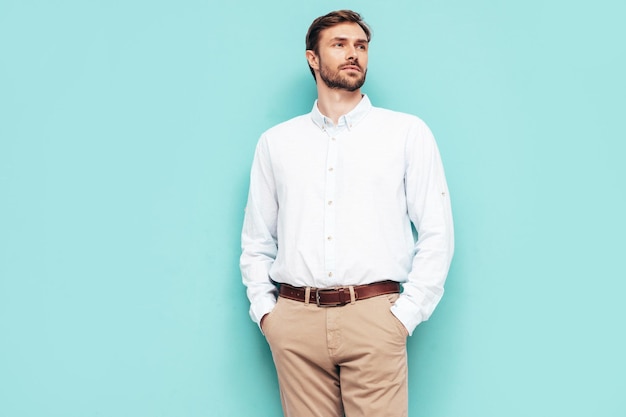 Free Photo portrait of handsome smiling model sexy stylish man dressed in shirt and trousers fashion hipster male posing near blue wall in studio isolated